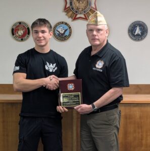 2024 Voice of Democracy winner for Post 3617, Kanyon Darnell, receiving a plaque from, and sharking hands with, Post Commander Brad Pieratt