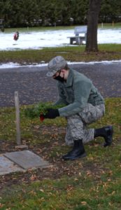 Civil Air Patrol cadet kneeling to place a wreath on a grave marker