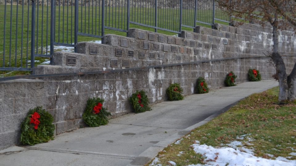 Series of wreaths along a wall with multiple grave markers