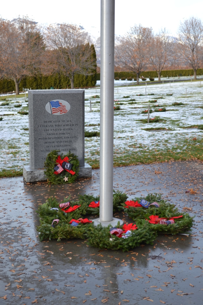 Wreaths surrounding base of flagpole, with one resting at base of Veteran Memorial marker in background