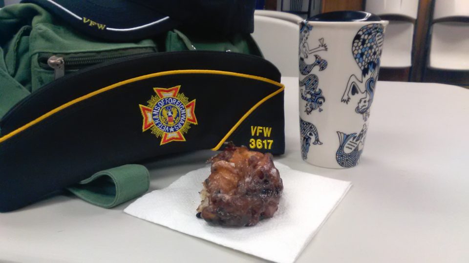 VFW Ladies Style cap, travel mug of coffee, and half of a blueberry fritter