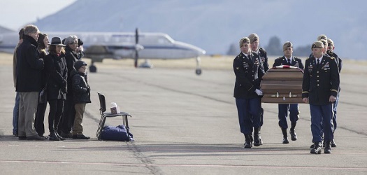 Casket of Sgt Jasso being carried on tarmac by military members while a small group watches