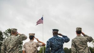 Armed Forces members in uniform saluting the American Flag