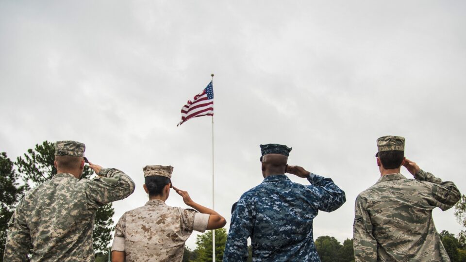 Armed Forces members in uniform saluting the American Flag