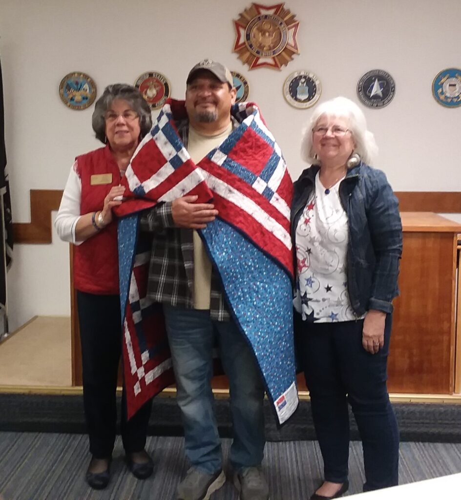 Two women have wrapped the standing veteran with the quilt.